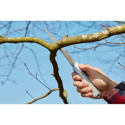 Stanley 0-10-129 folding saw cutting tree branch outdoors, silver handle, product photography.