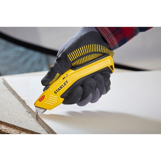 STANLEY 0-10-237 utility knife cutting drywall, close-up, held by gloved hand.