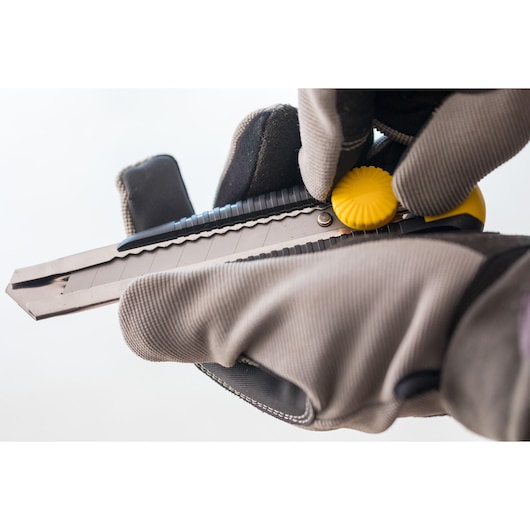 Photo of STANLEY 0-10-418 utility knife being adjusted with gloves, close-up on yellow dial and blade.