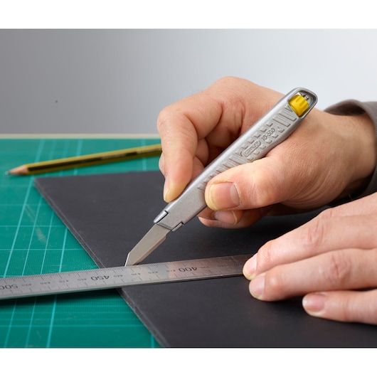 Photo of STANLEY 0-10-590 utility knife cutting black board with ruler on green mat.