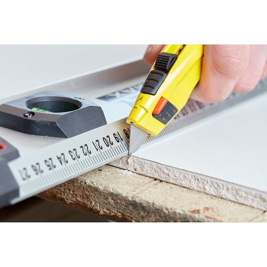 STANLEY 0-10-778 utility knife used to cut drywall along a metal ruler, close-up angle.