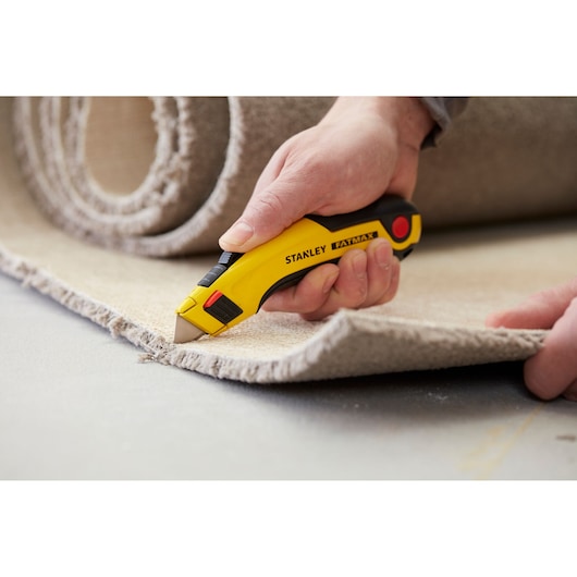 Stanley 0-10-778 utility knife cutting carpet, close-up photo, yellow and black handle, FatMax model.