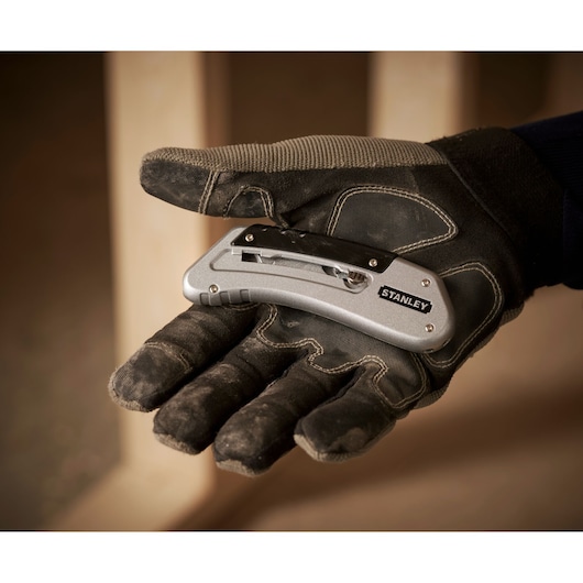 STANLEY 0-10-810 folding utility knife held in a gloved hand, silver with black clip, side view.
