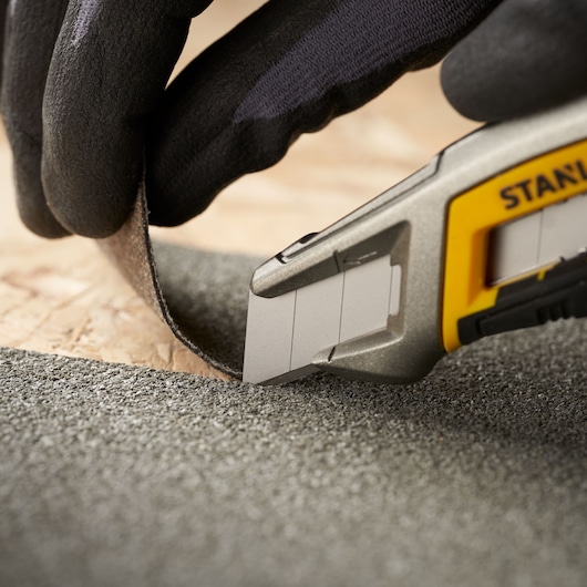 Photo of STANLEY 0-11-718 utility knife cutting roofing material, close-up with glove for detailed view.