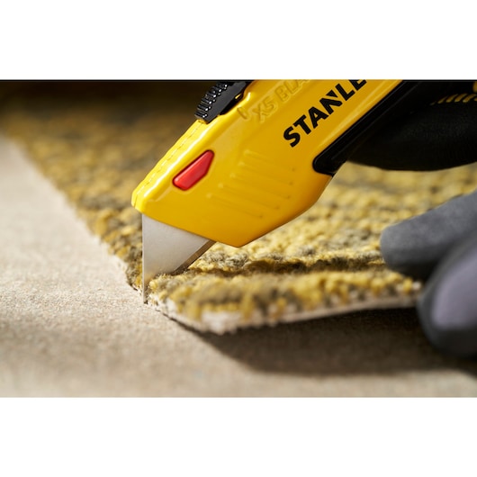 STANLEY 0-11-921 utility knife cutting yellow carpet, close-up photography of blade and handle.