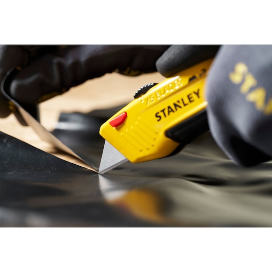STANLEY 0-11-921 utility knife with yellow handle cutting black material, close-up in use.