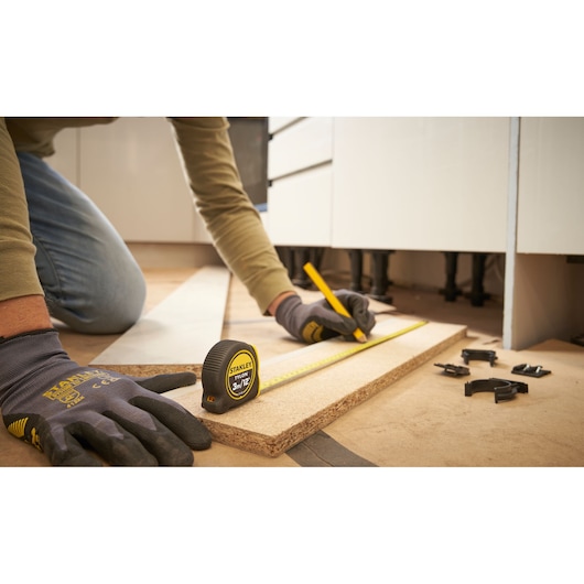STANLEY 0-30-686 tape measure on wood plank, person measuring and marking with pencil, close-up workshop scene.