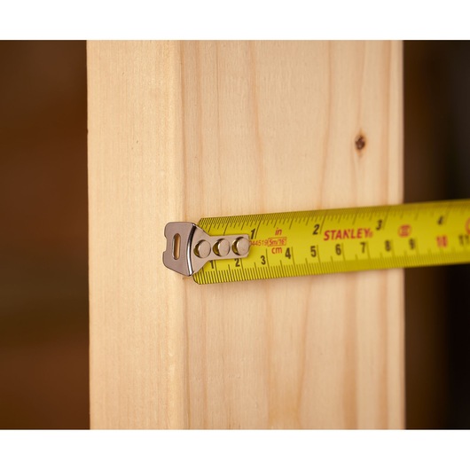 STANLEY 0-33-553 tape measure in use measuring wooden plank, close-up side angle.