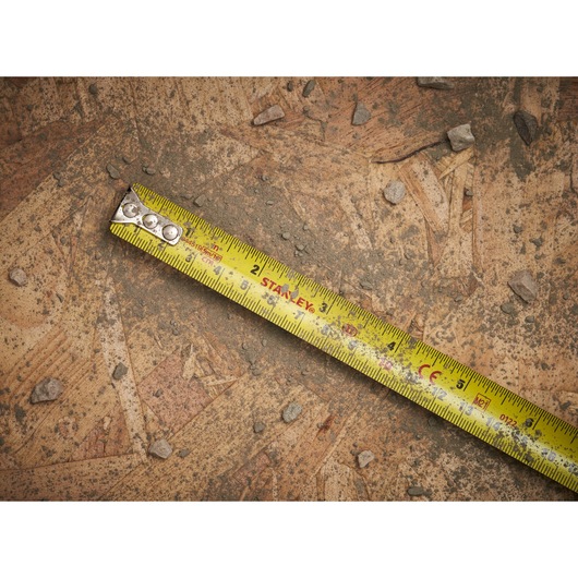 STANLEY 0-33-553 tape measure showing yellow blade with black markings, placed on a dirty wooden surface.