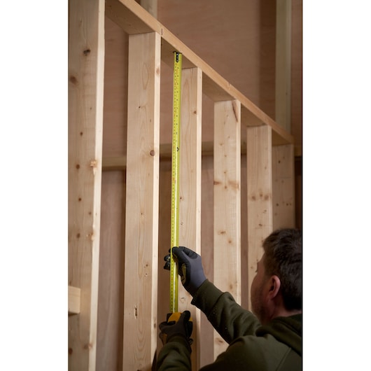 STANLEY 0-33-726 tape measure used by a person to measure vertical wooden beams, close-up action photo.