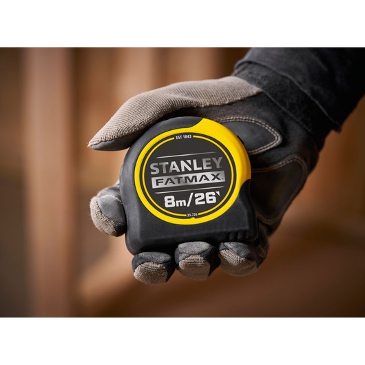 STANLEY 0-33-726 tape measure FATMAX, black and yellow, 8m/26ft, close-up held in a gloved hand.