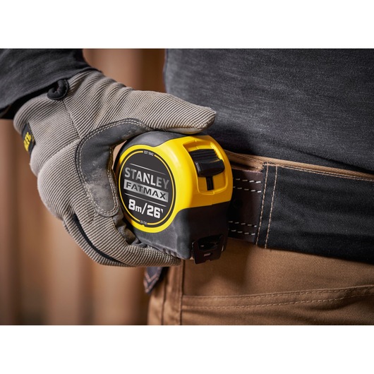 Photo of STANLEY 0-33-726 tape measure, yellow and black, clipped to a tool belt, worker wearing gloves.
