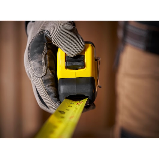 Photo of STANLEY 0-33-726 tape measure in gloved hand, yellow and black casing, measuring tape extended.