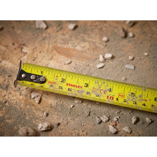 STANLEY 0-33-726 tape measure with yellow blade on a dusty, rocky surface, close-up showing measurements.