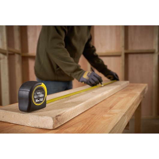 STANLEY 0-33-805 tape measure on wood plank, workshop setting, person marking measurement.