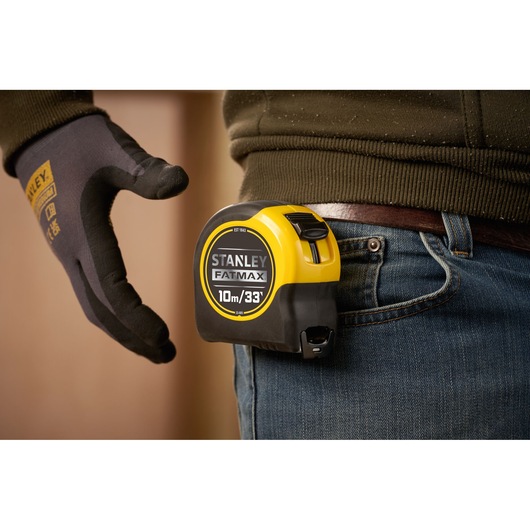 STANLEY 0-33-805 tape measure clipped to jeans, FATMAX branding visible, side view, hand wearing work glove.