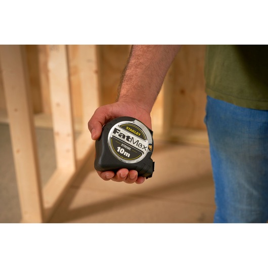 STANLEY 0-33-897 tape measure FatMax Xtreme 10m held in hand, construction background.