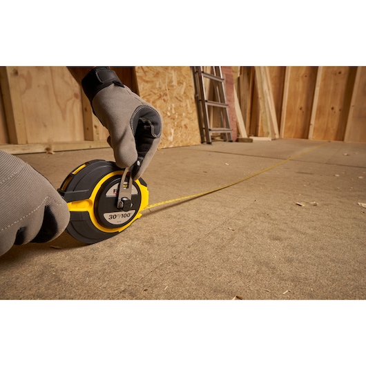 Photo of STANLEY 0-34-132 long tape measure in use on construction floor, yellow and black casing, gloved hand visible.