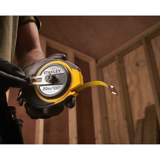 Photo of STANLEY 0-34-132 FatMax 30m/100ft tape measure held by a person wearing gloves.