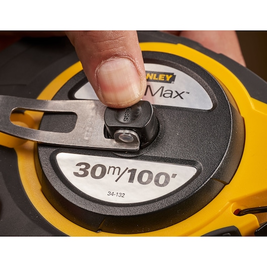 Photo of STANLEY 0-34-132 tape measure with a finger pressing the locking button, close-up view.