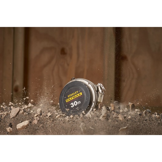 STANLEY 0-34-203 tape measure, 30m FATMAX, rugged design shown in action with dirt and rocks in the foreground.