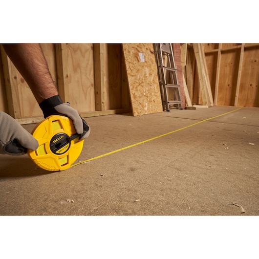 Photo of STANLEY 0-34-262 long tape measure, yellow casing, extended on construction floor.