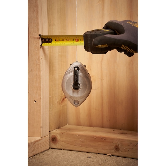 STANLEY 0-47-100 chalk line tool in use, hanging vertically with a hand measuring distance, construction setting.