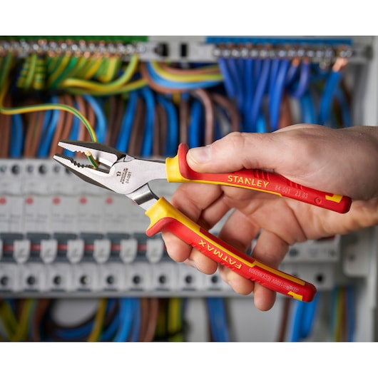 Photo of STANLEY 0-84-001 insulated pliers held by hand near electrical wiring, yellow and red handles.