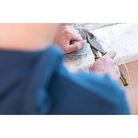 STANLEY 0-89-859 pliers cutting wire, close-up photo with spool of wire on work surface.