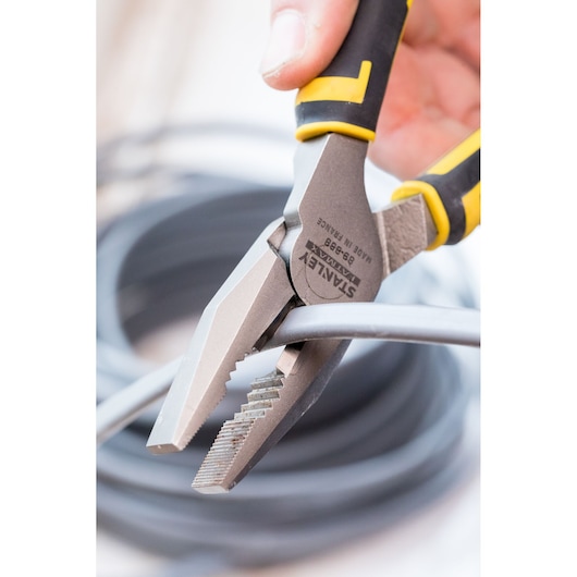 STANLEY 0-89-868 combination pliers with yellow and black handle cutting a gray cable, close-up.