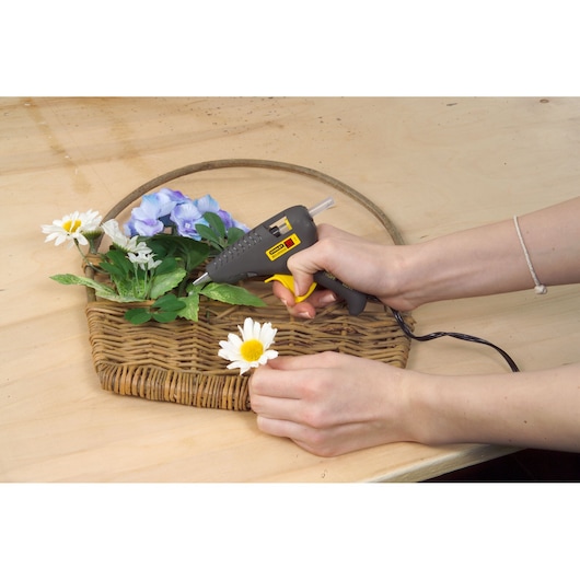 STANLEY 0-GR15 glue gun used to attach flowers to a wicker basket on a wooden table, front angle.