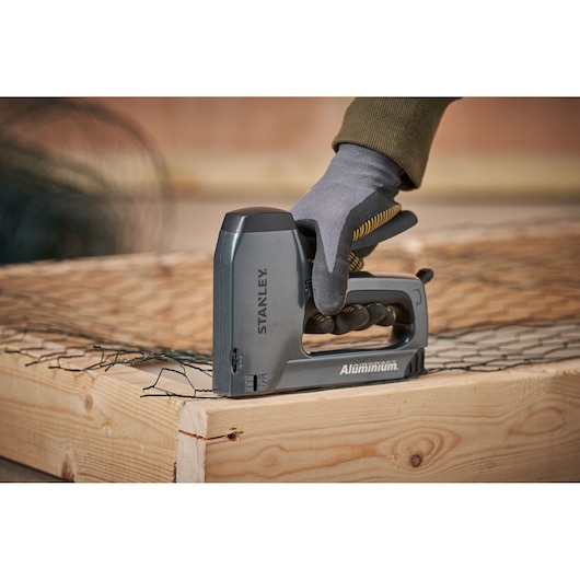 Stanley 0-TR250 aluminum stapler in use securing wire mesh on wooden frame, product side view.