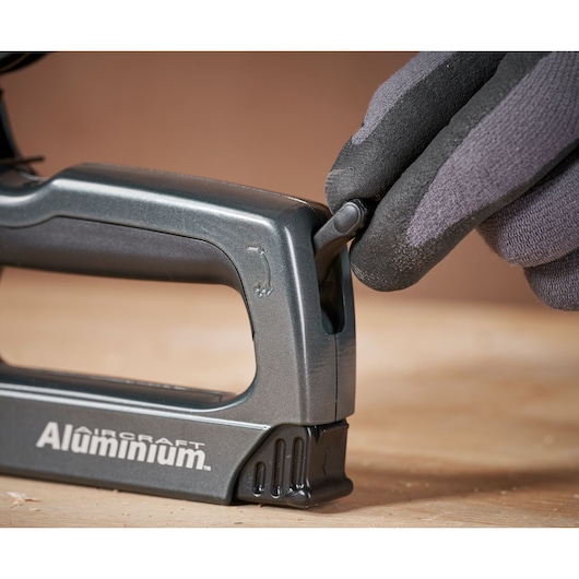 STANLEY 0-TR250 stapler side view, black glove adjusting lever, silver body, product on wood surface.