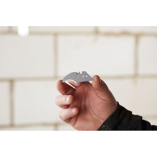 Stanley 1-11-952 utility knife blade held in hand, photography category, construction background.