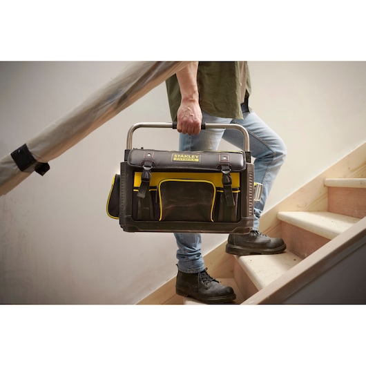 STANLEY 1-79-213 tool bag in black and yellow, photographed being carried up stairs by a person.