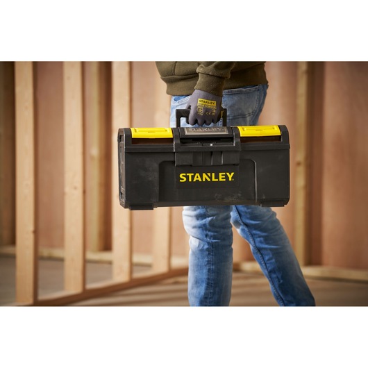Photo of STANLEY 1-79-217 black and yellow toolbox being carried by a person wearing gloves at a jobsite.