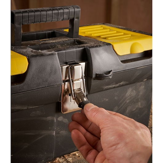 A close-up of a person's hand opening the metal latch on a black and yellow STANLEY toolbox.