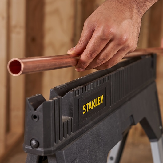 Photo of STANLEY 1-92-980 sawhorse holding a copper pipe, close-up of hand positioning the pipe.