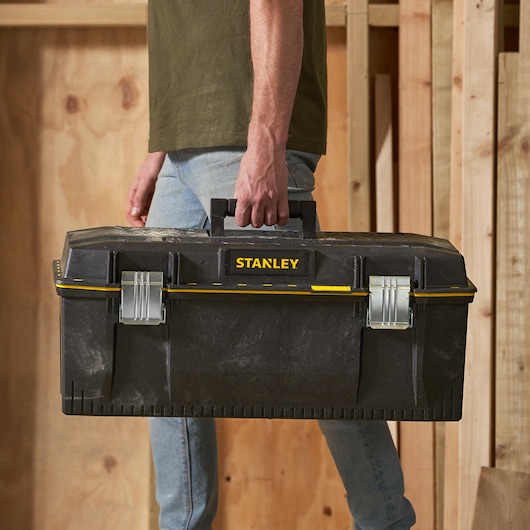 Photo of STANLEY 1-93-935 black toolbox with yellow accents, being carried by handle, front angle.