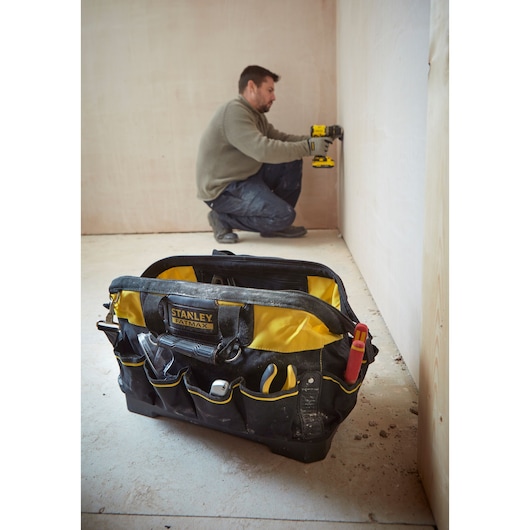 Photo of STANLEY 1-93-950 tool bag with tools, foreground on construction site, worker in background.