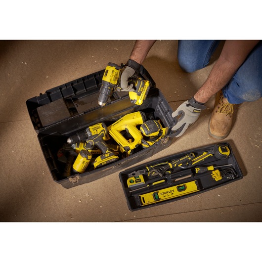 STANLEY 1-94-859 toolbox with yellow power tools and hand tools, top-down angle, on workshop floor.
