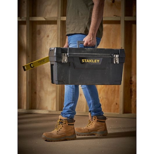 Photo of STANLEY 1-94-859 toolbox being carried, with STANLEY level protruding from side, indoor construction setting.