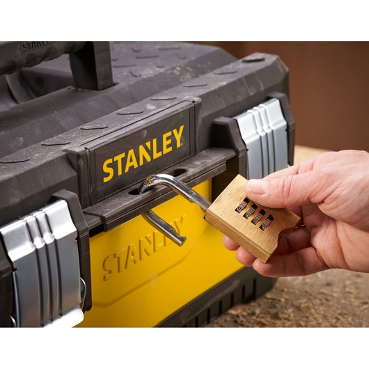 A close-up of a hand unlocking a combination padlock attached to a black and yellow STANLEY toolbox.