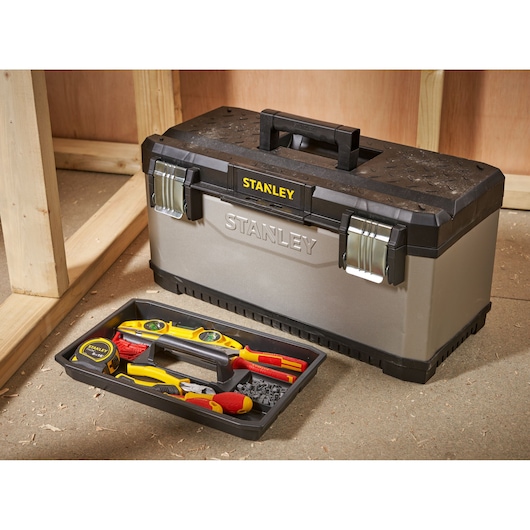 Stanley toolbox with a removable tray containing various hand tools, placed on a workshop floor near wooden framing.