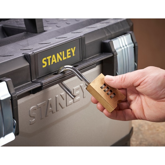 A hand unlocking a STANLEY toolbox with a brass combination padlock.