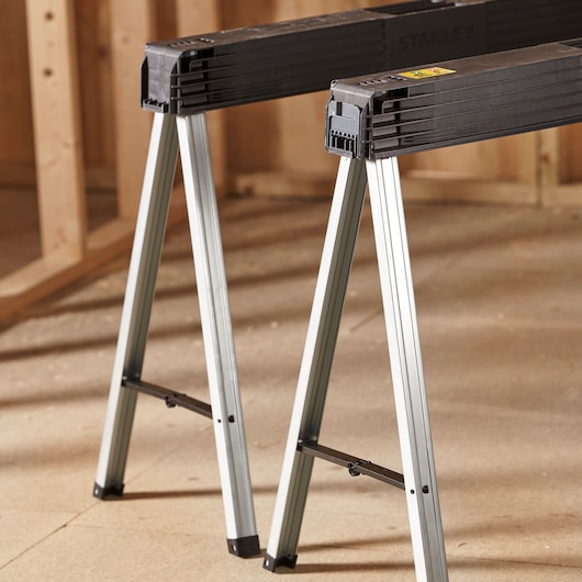 STANLEY 1-97-475 metal and plastic sawhorse, side angle, shown in a workshop setting.