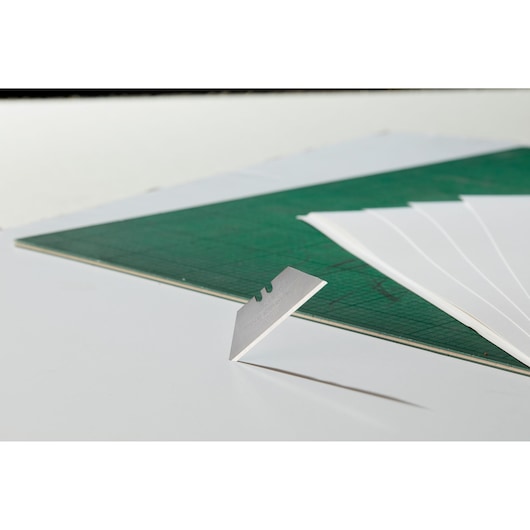 STANLEY 1-98-460 razor blade upright on green cutting mat with sheets, side angle, photography product.