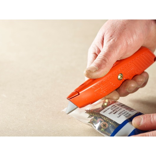STANLEY 2-11-987 utility knife cutting plastic screw packaging, close-up showing orange handle and blade.