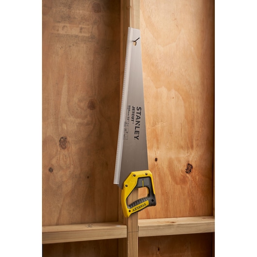 STANLEY 2-15-289 hand saw with yellow and black handle hanging on wooden stud, side angle.