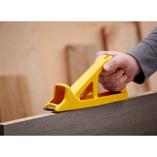 STANLEY 5-21-103 hand rasp tool in yellow, shown smoothing wood surface in close-up photography.